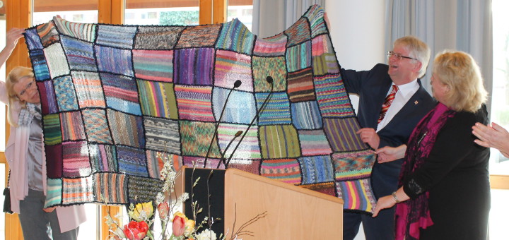 Bürgermeister Thomsen präsentiert die Patchwork-Decke, die von neuen und alten Stuhrer Bürgern gestrickt wurde.