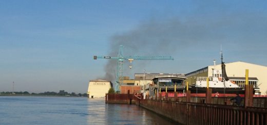 Auch am Freitagmorgen, Stunden nachdem das Feuer ausgebrochen ist, steht noch eine Rauchwolke über der Lürssen Werft. Foto: Harm