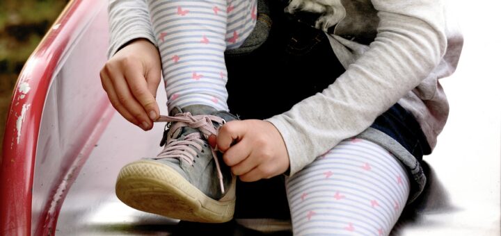 Auf dem Bild sieht man ein Kind dass sich die Schuhe zuschnürt.